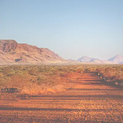 Landschaftsbild Australien mit Hügeln in der Ferne und einem langen, rötlichen Weg.